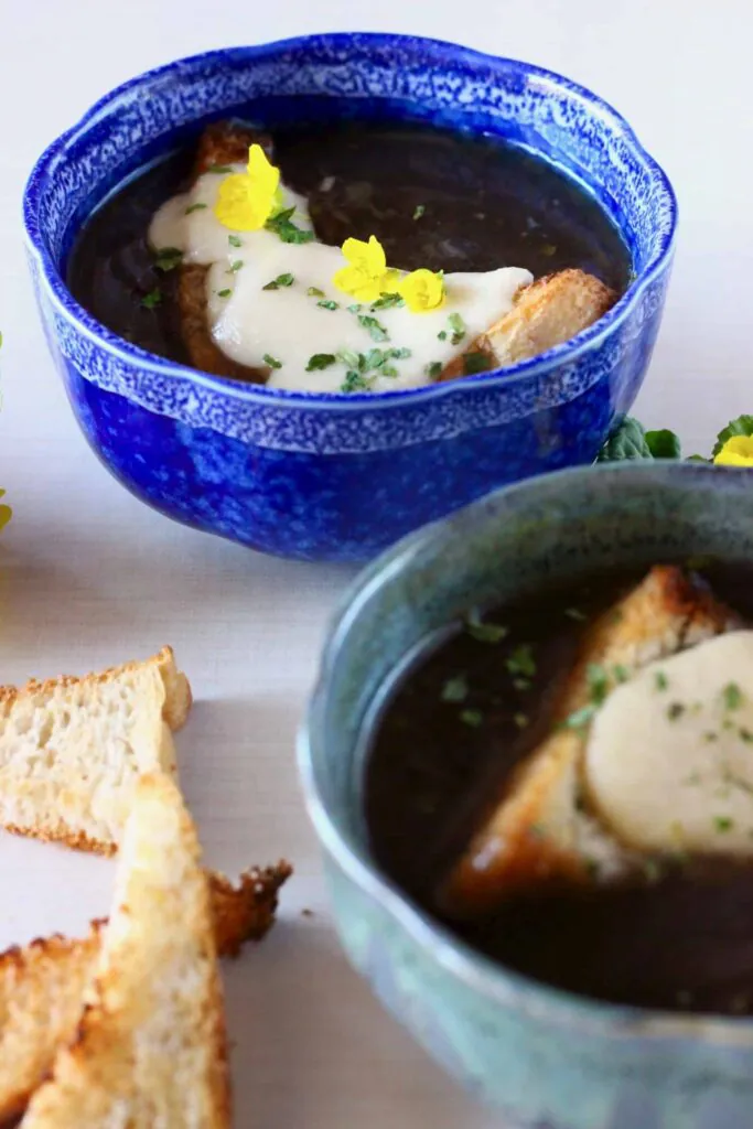Photo of two blue bowls filled with dark brown soup topped with cheese on toast