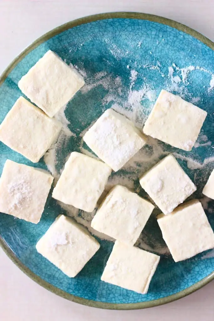 Cubes of tofu coated in cornflour on a blue plate against a white background