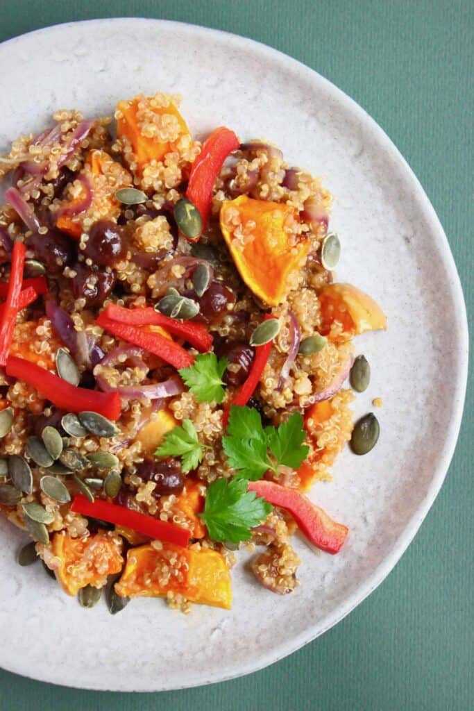 Photo of quinoa, roasted pumpkin and sliced red pepper salad on a grey plate against a dark green background