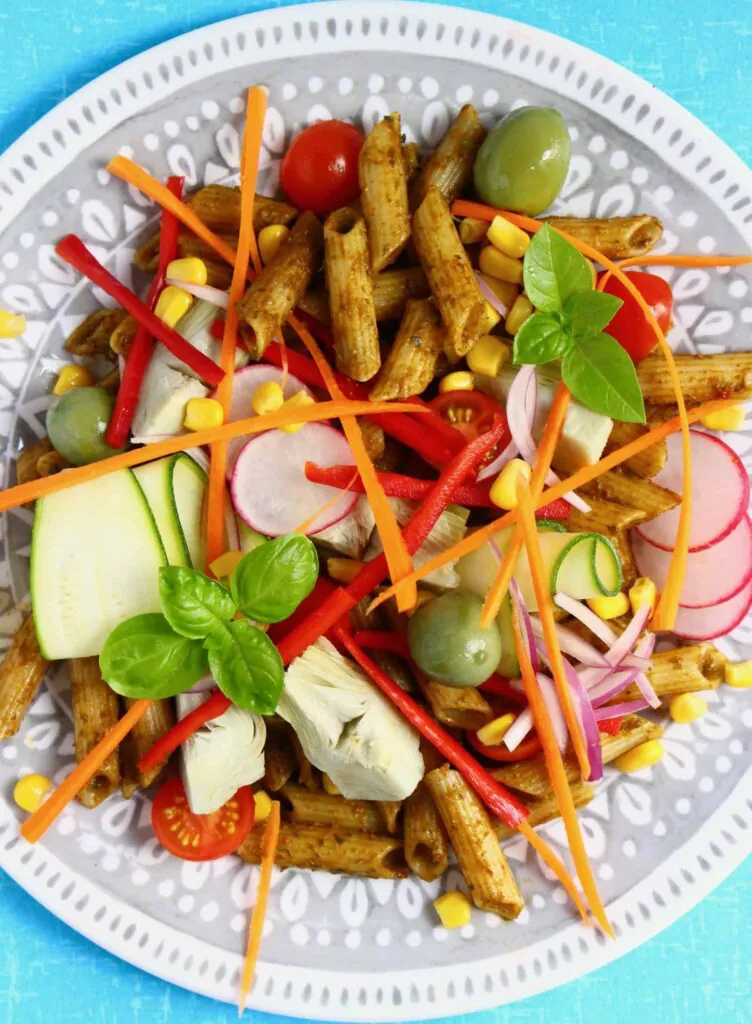 Penne pasta with red pesto and fresh vegetables on a grey plate 