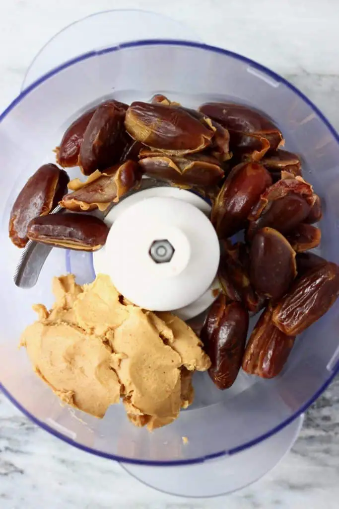 Dates, almond butter and salt in a food processor against a marble background