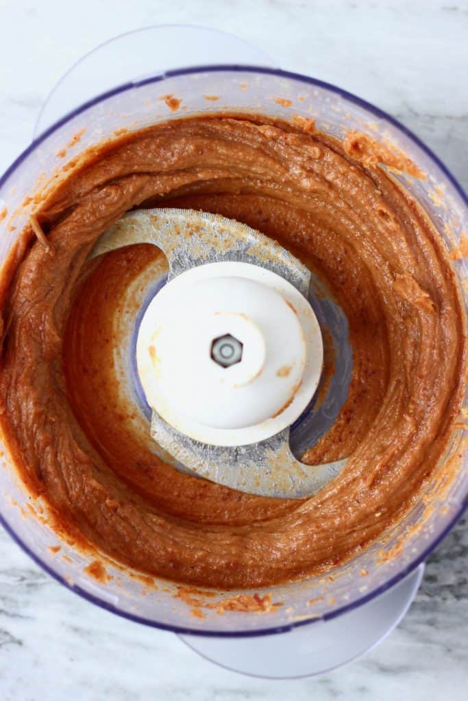 Blended-up dates and almond butter in a food processor against a marble background