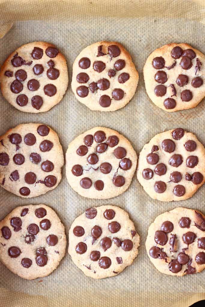 Nine chocolate chip cookies on a baking tray lined with brown baking paper