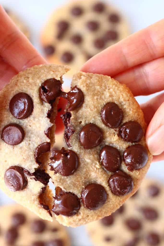 A chocolate chip cookie broken in half being held up by two hands