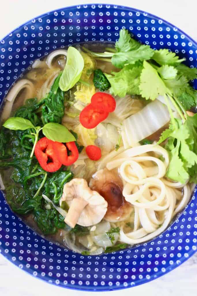 Rice noodles and vegetables in a soup in a dark blue bowl