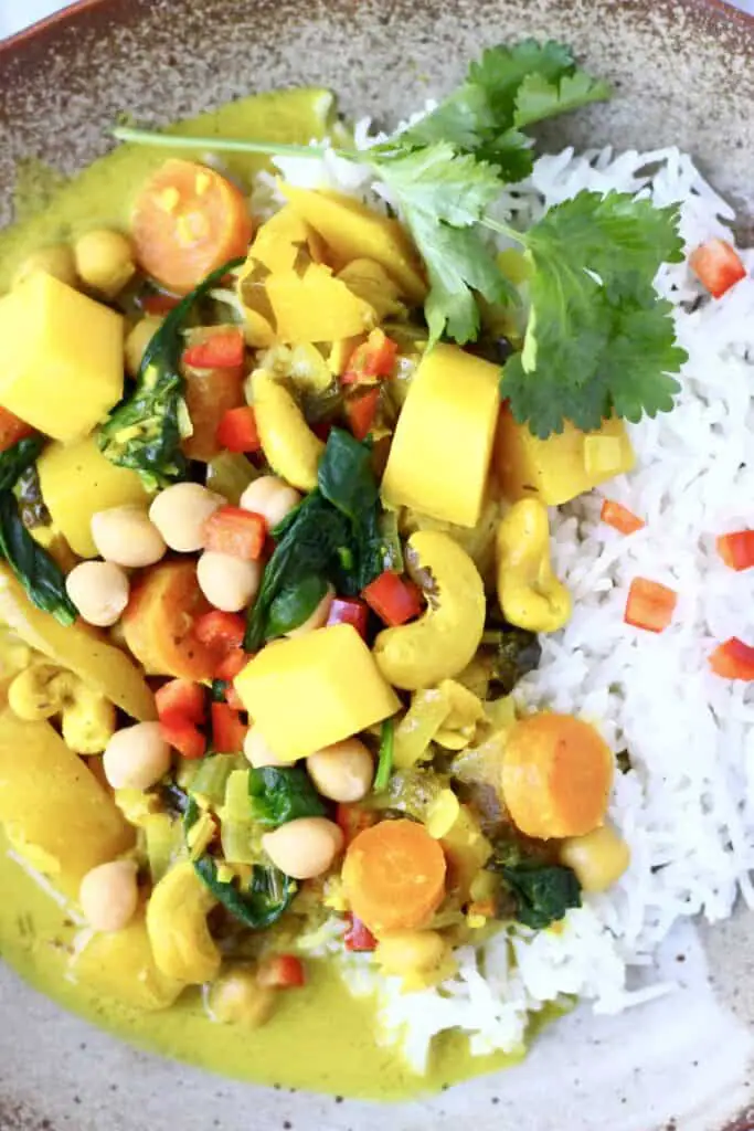 Curry made with mango, cashew nuts, spinach and chickpeas with white rice on a brown plate against a marble background