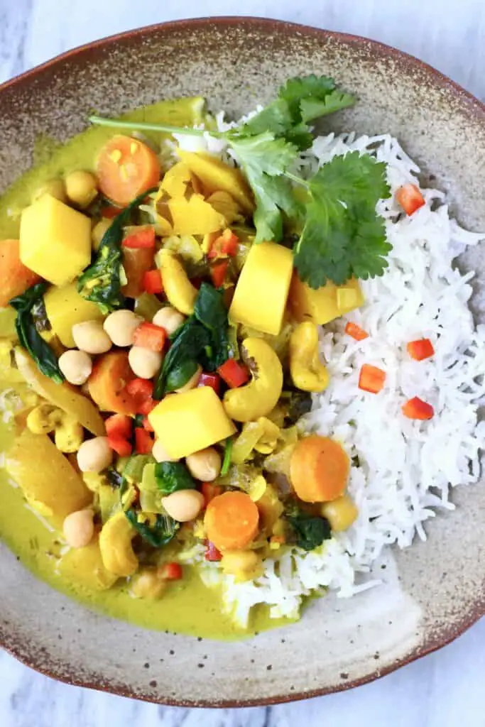 Curry made with mango, cashew nuts, spinach and chickpeas with white rice on a brown plate against a marble background