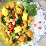 Curry made with mango, cashew nuts, spinach and chickpeas with white rice on a brown plate