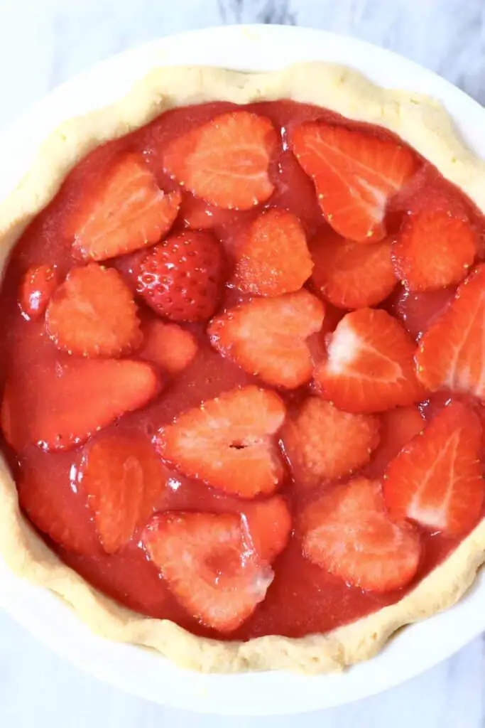 Photo of a strawberry pie in a white pie dish against a marble background