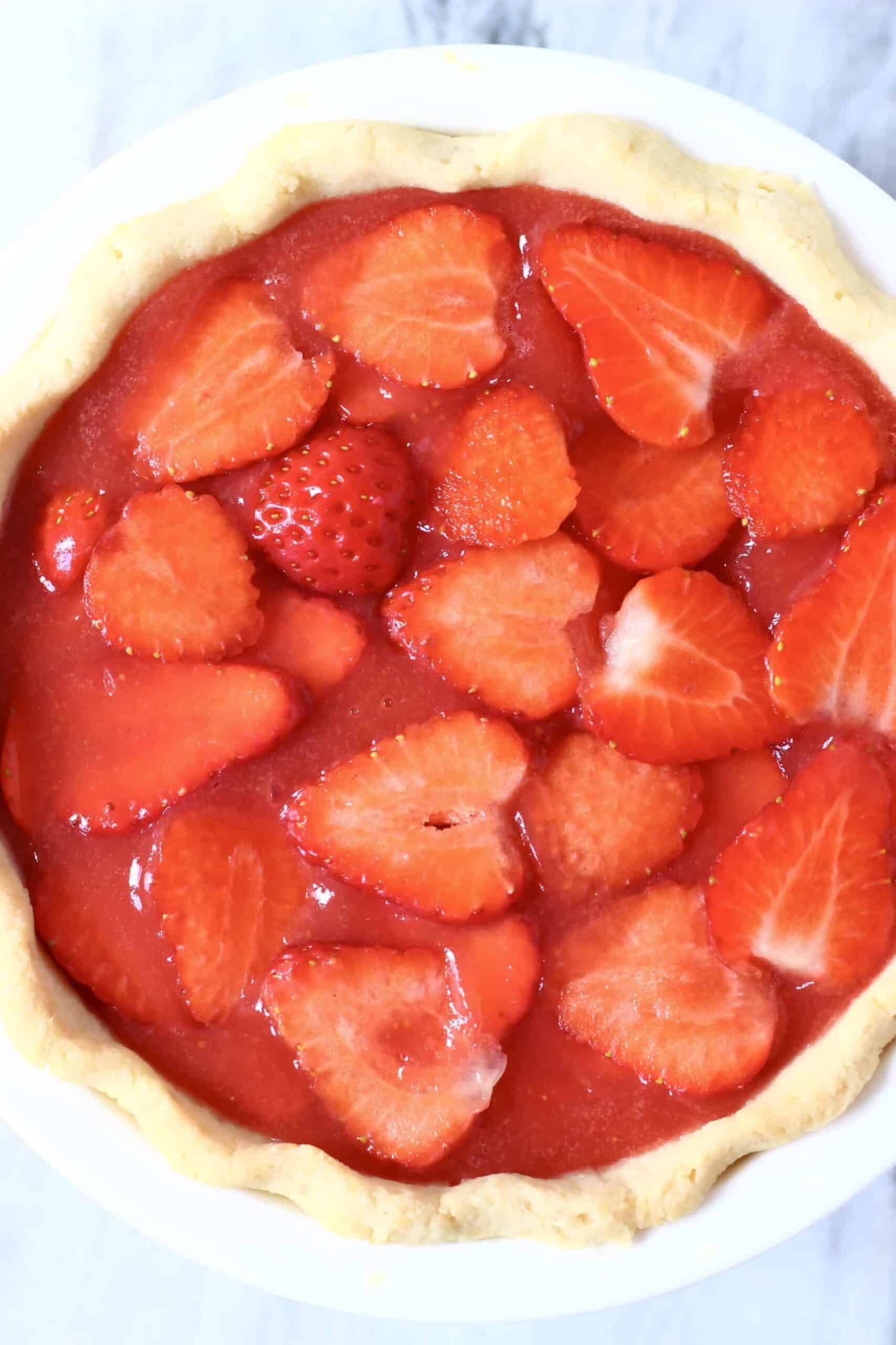 This Gluten-Free Vegan Strawberry Pie is crispy and flaky, fresh and fruity, and sweet and juicy! Refined sugar free and naturally coloured. A pie crust filled with sliced strawberries and agar fresh strawberry jelly. Perfect for summer entertaining - BBQs, potlucks, picnics, baby showers etc. #vegan #glutenfree #dairyfree #plantbased #pie #dessert #strawberry #summer Photo of a strawberry pie in a white pie dish against a marble background