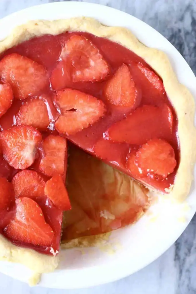 Photo of a strawberry pie with a slice cut out of it in a white pie dish