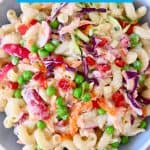 Pasta salad with green peas, shredded cabbage, radish and carrots in a mayonnaise dressing in a light blue bowl against a marble background