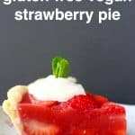 A slice of strawberry pie topped with white cream and a sprig of mint on a white plate with pink flowers against a grey background