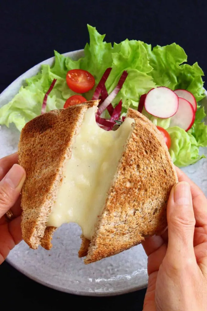 A toasted grilled cheese sandwich being pulled apart by two hands against a grey plate with lettuce