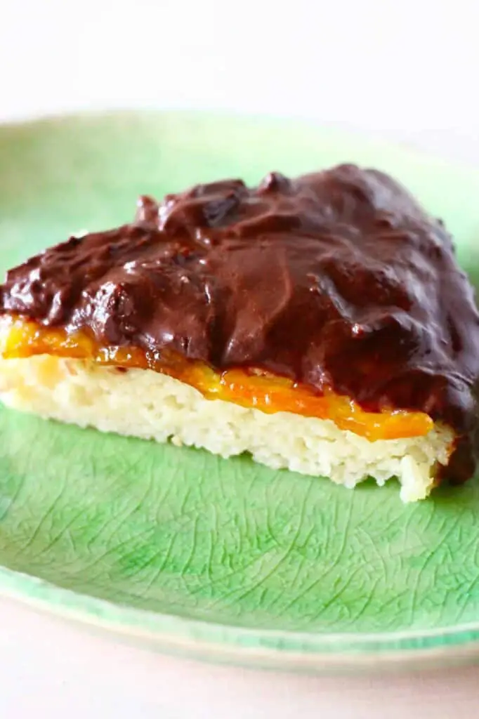 Photo of a slice of sponge cake topped with orange marmalade and chocolate ganache on a green plate