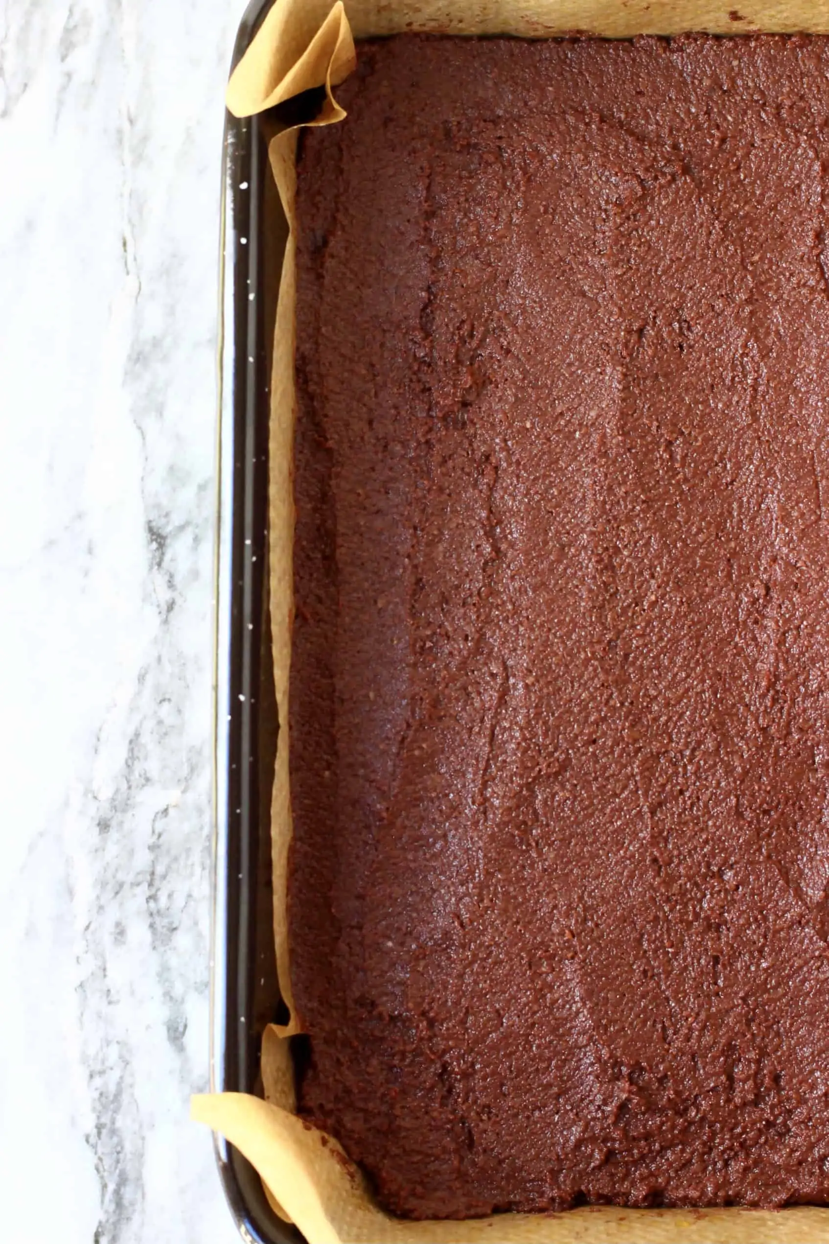 Raw vegan gluten-free chocolate brownie batter in a square baking tin lined with baking paper