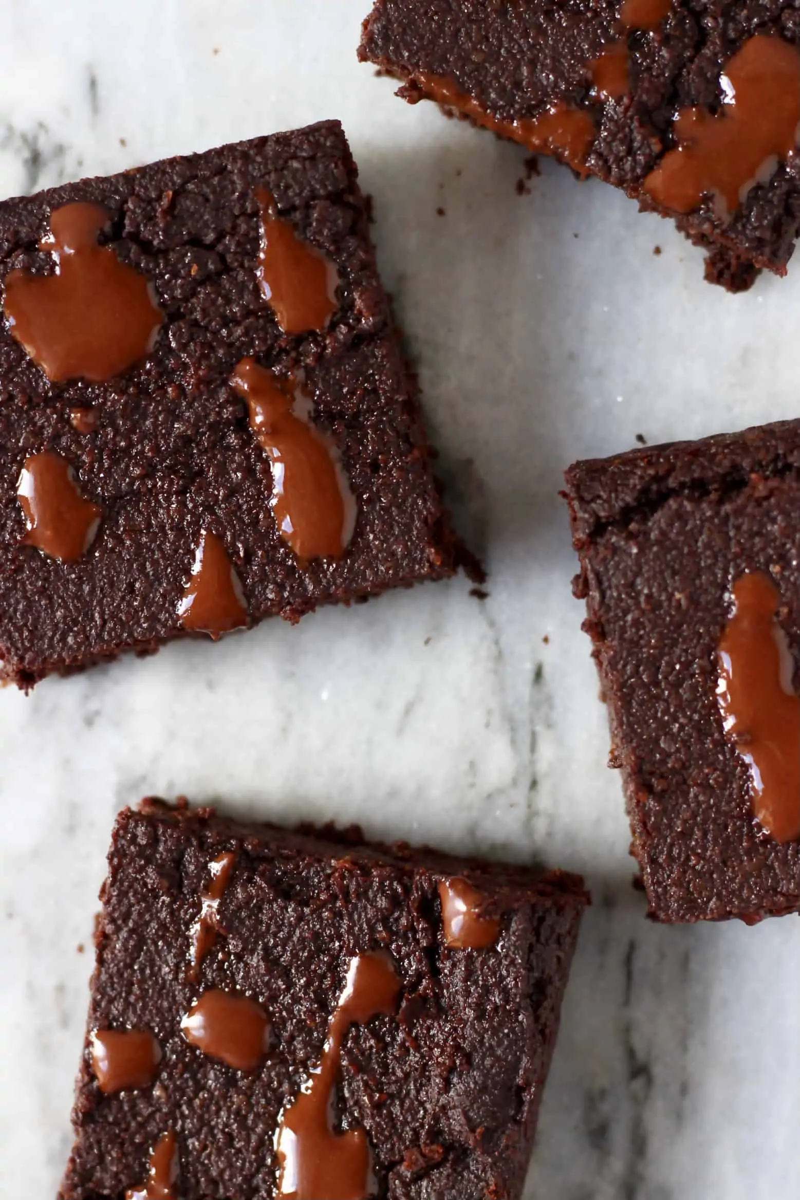 Four square vegan gluten-free chocolate brownies on a marble background