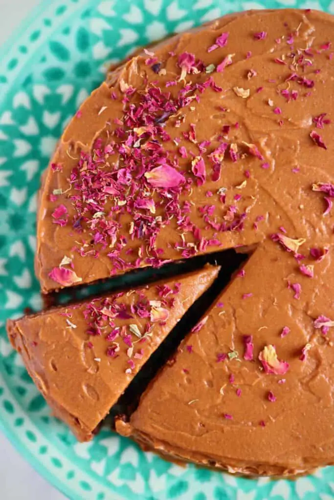 Photo of a chocolate cake covered in chocolate buttercream topped with rose petals on a blue cake stand taken from above