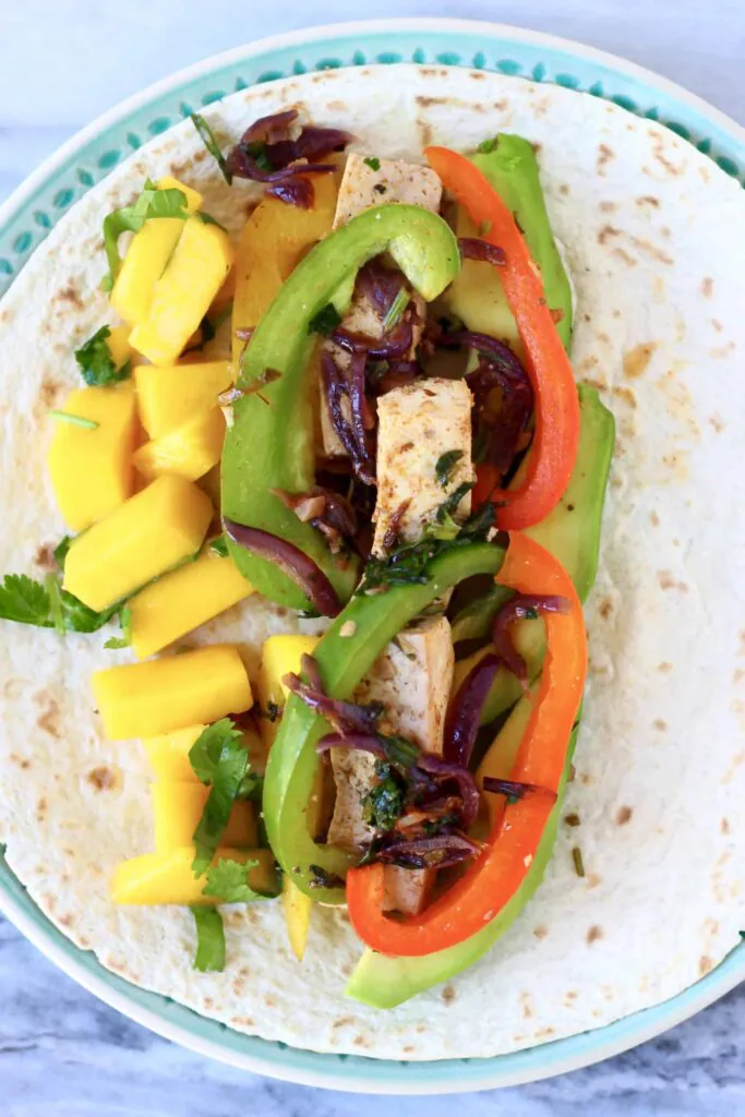 Tofu, sliced peppers and diced mango on a tortilla on a blue plate