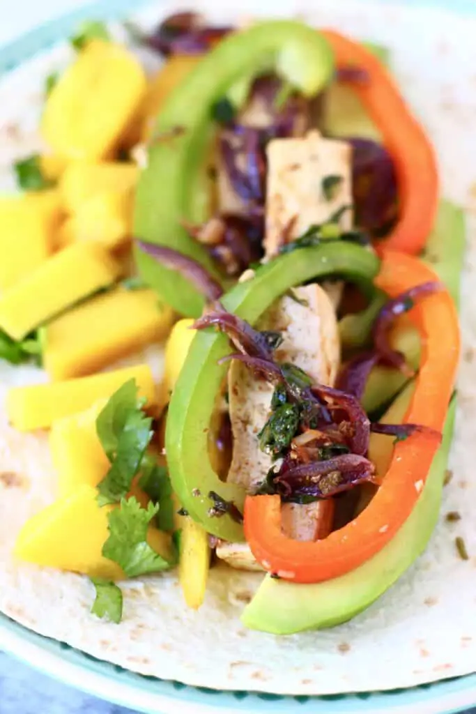Tofu, sliced peppers and diced mango on a tortilla on a blue plate