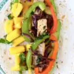 Tofu, sliced peppers and diced mango on a tortilla on a blue plate