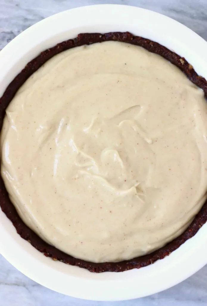 Photo of a brown chocolate pie crust filled with light brown peanut butter filling in a white pie dish against a marble background