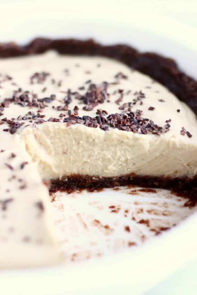 Photo of a sliced pie in a white pie dish - a brown chocolate crust with a light brown filling and sprinkled with cacao nibs