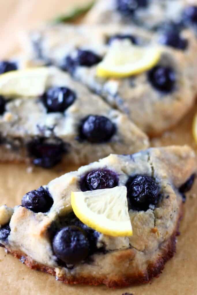 Three gluten-free blueberry scones topped with lemon wedges on a sheet of brown baking paper