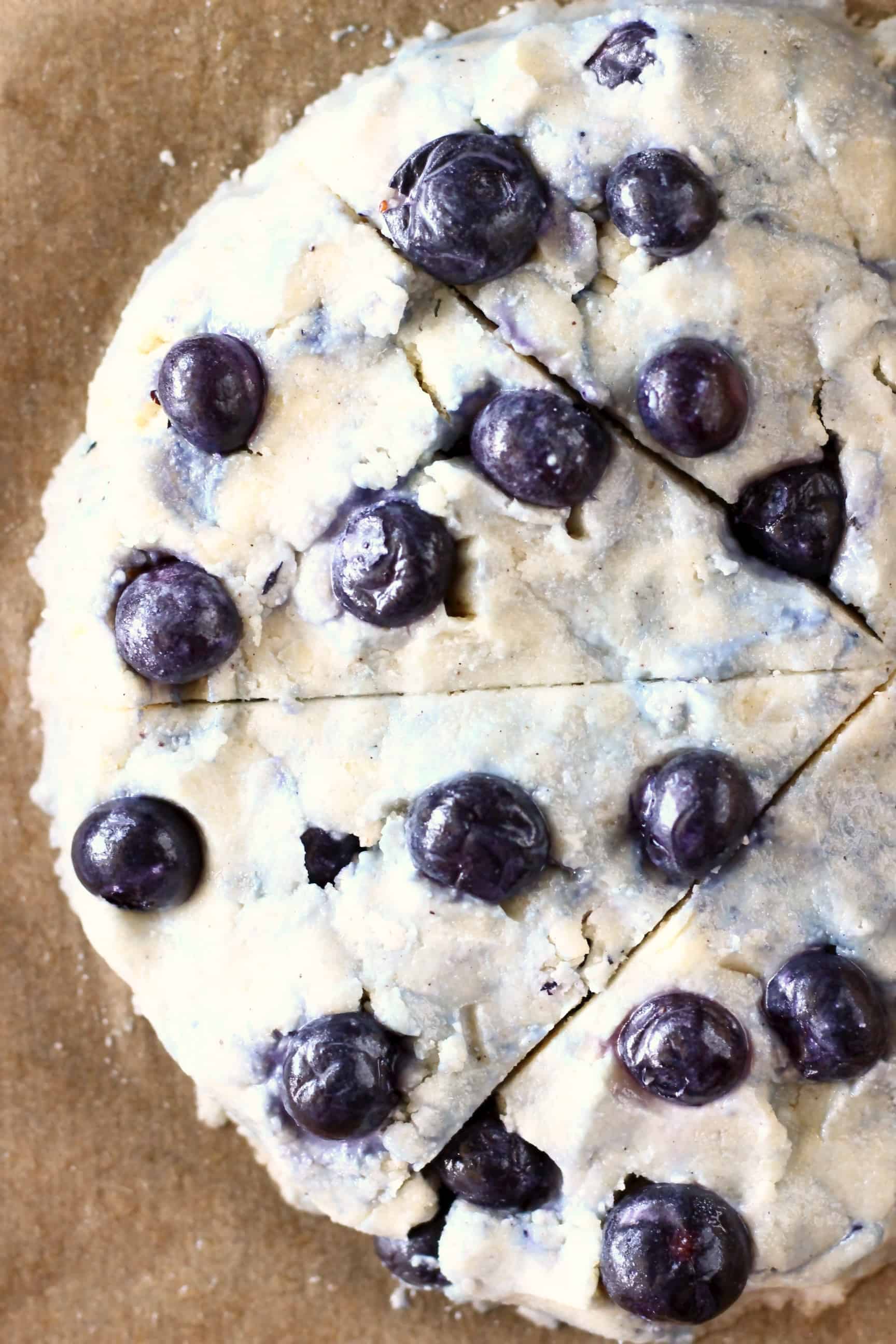 Raw gluten-free blueberry scone dough on a sheet of brown baking paper 