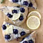 Four triangular blueberry scones topped with lemon wedges on a sheet of brown baking paper