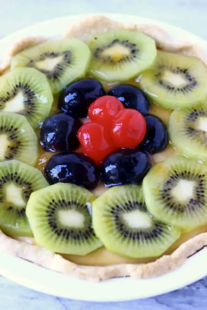 Photo of a fruit tart topped with sliced kiwis, grapes and red cherries in a white pie dish