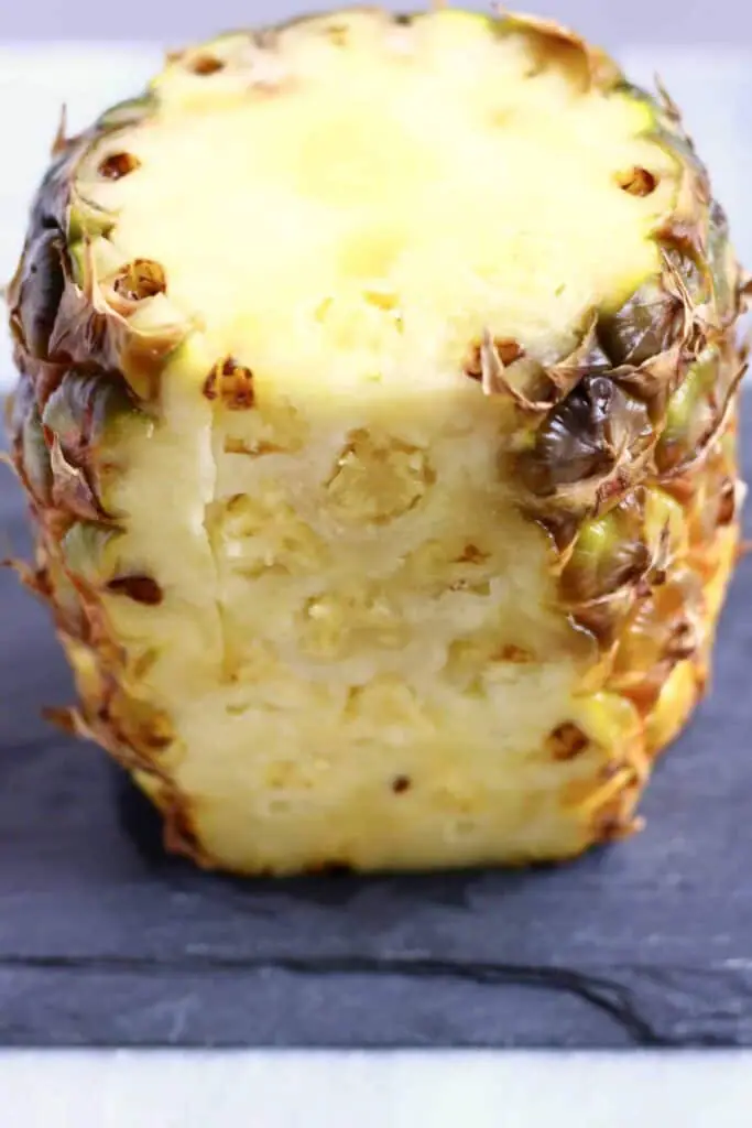 Photo of a vertical pineapple with the top and half of the skin cut off on a black slab
