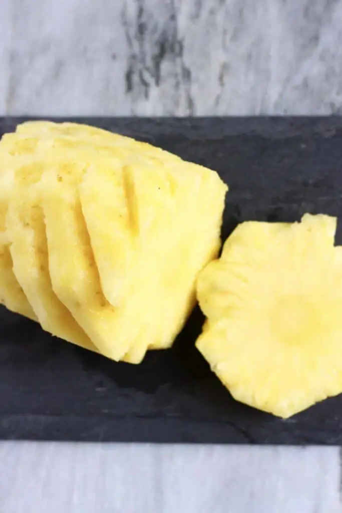 Photo of a sliced pineapple on a black slab against a marble background