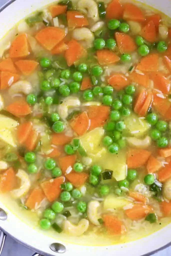 Photo of a saucepan with raw rice, green peas, carrots, pineapple chunks and water