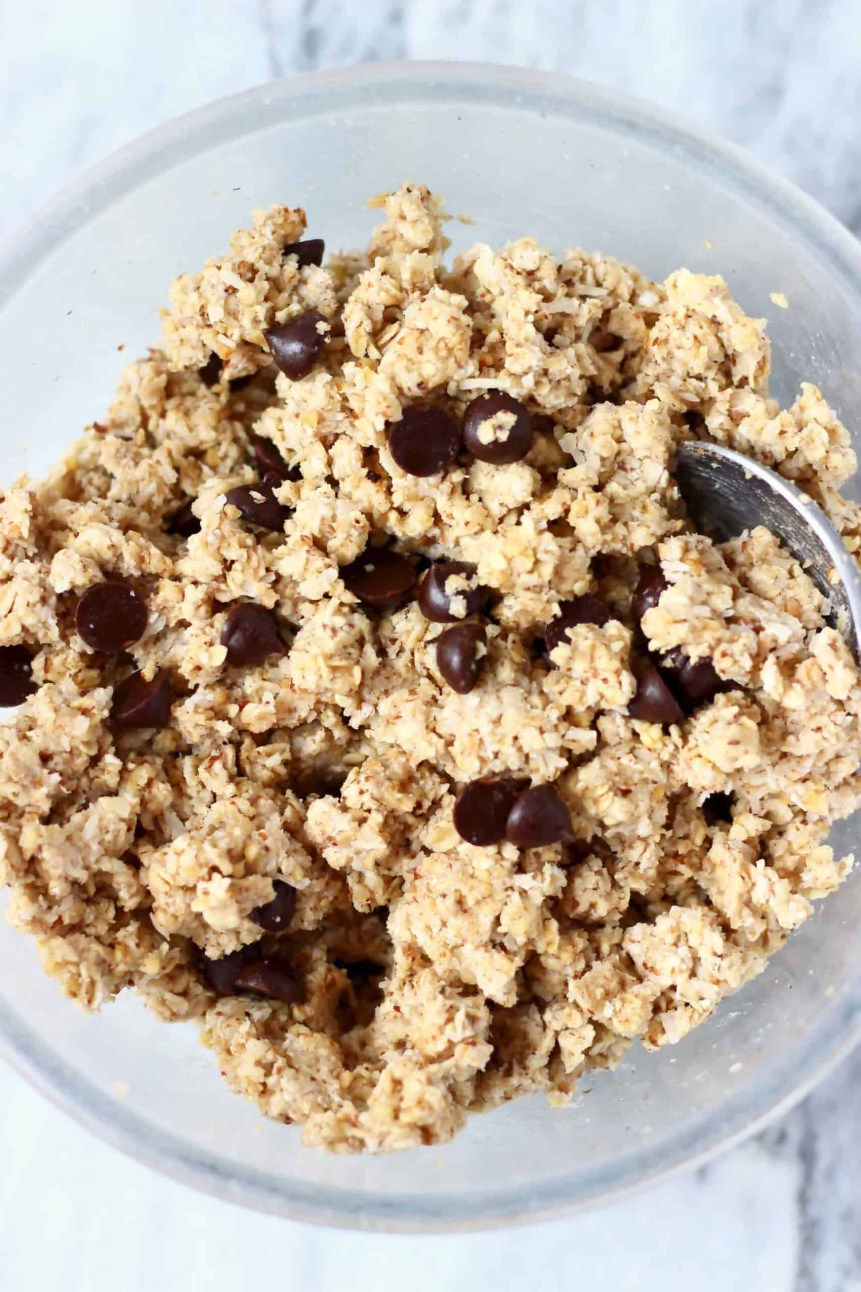 Photo of chocolate chip cookie dough in a glass mixing bowl with a silver spoon against a marble background