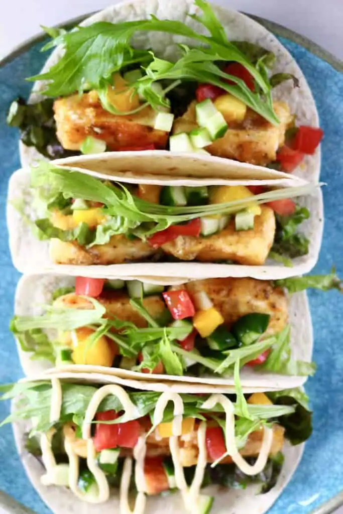 Photo of four tortillas stuffed with crispy tofu, mango, tomato, cucumber and lettuce on a blue plate