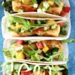 Photo of four tortillas stuffed with crispy tofu, mango, tomato, cucumber and lettuce on a blue plate