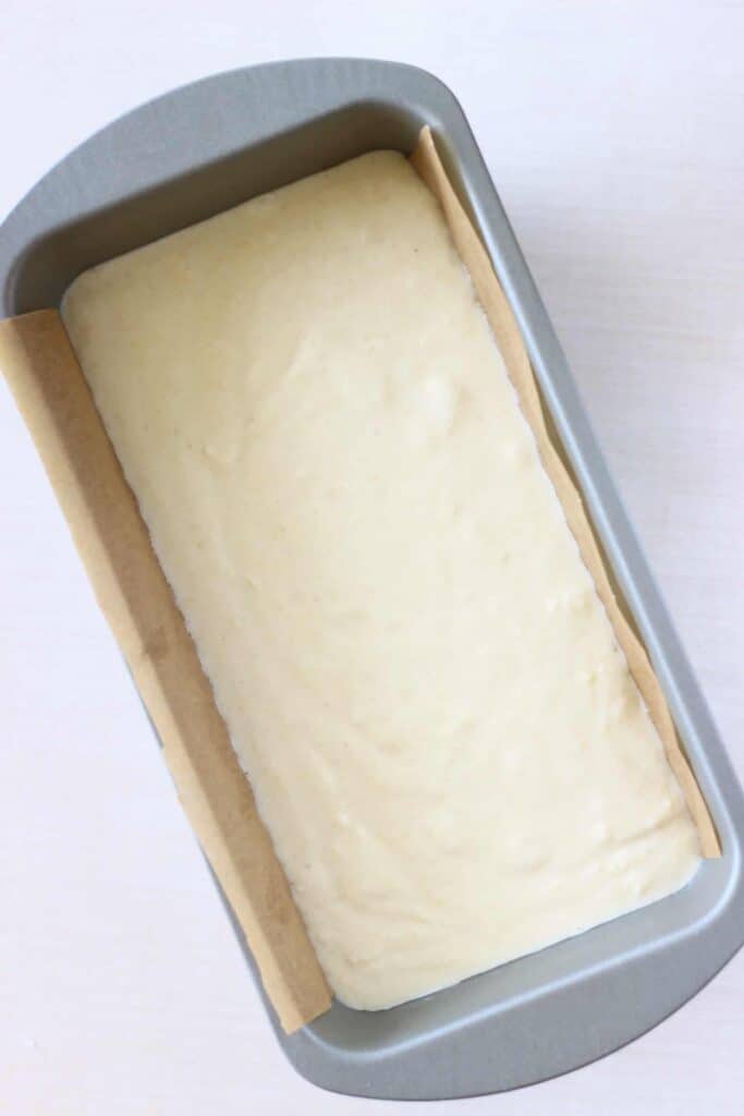 Photo of raw cake batter in a silver loaf tin against a white background