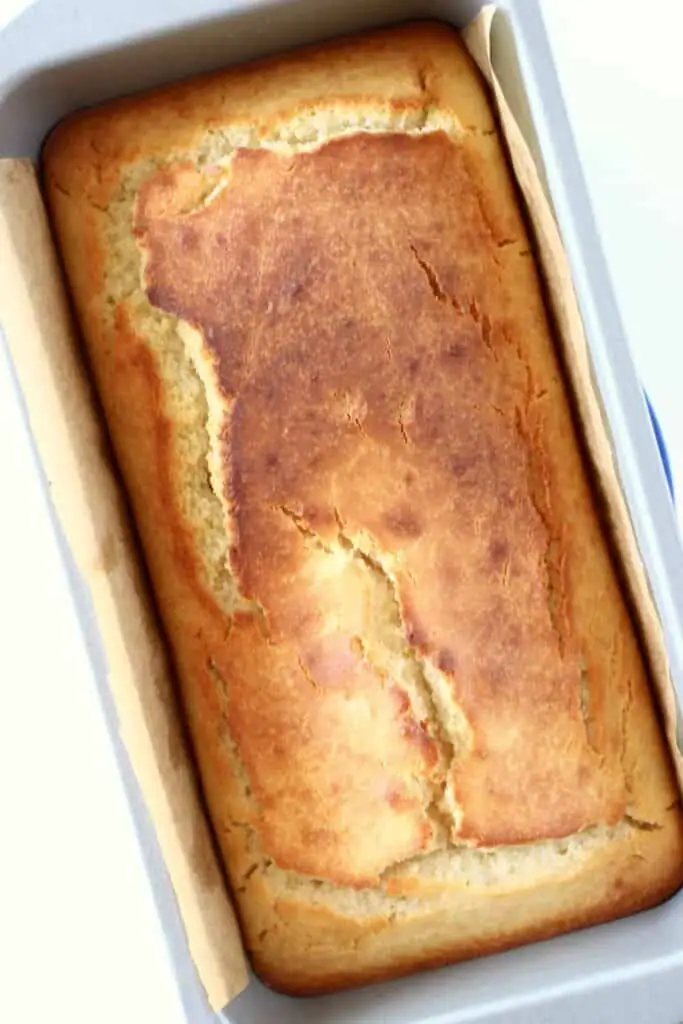 Photo of a golden brown pound cake in a silver loaf tin against a white background