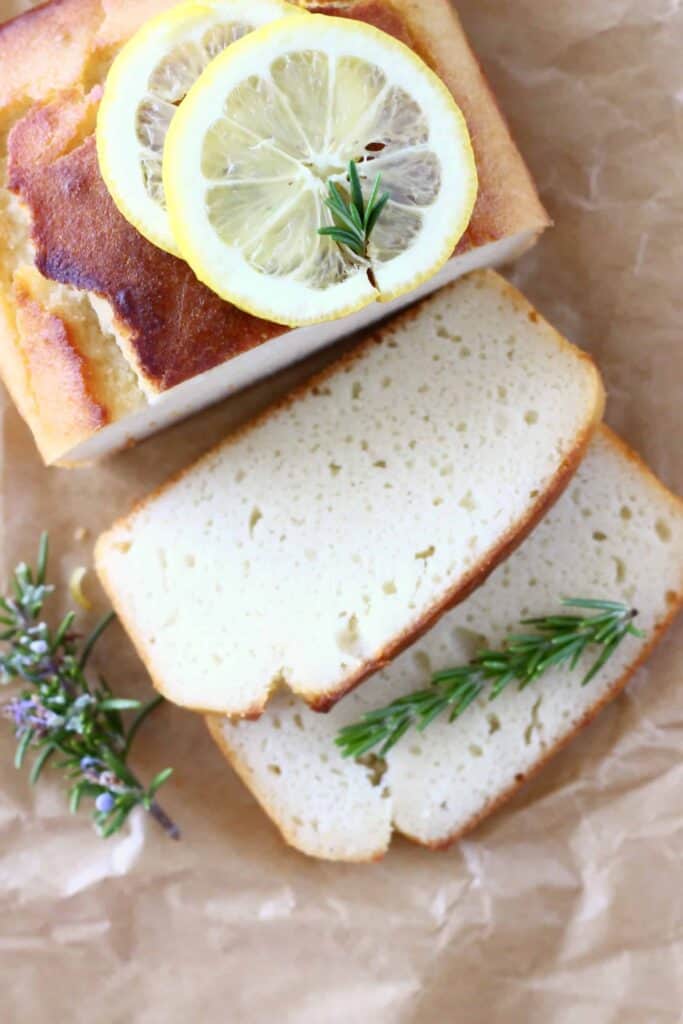 Photo of a golden brown pound cake topped with lemon slices with two white slices of cake next to it on top of brown baking paper