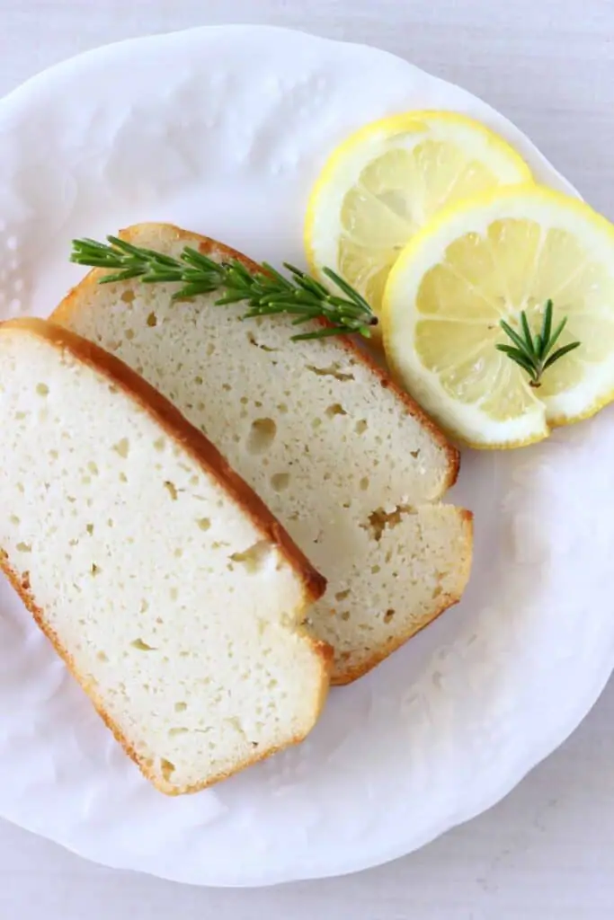 Two slices of white cake on a white plate with lemon slices and a sprig of rosemary