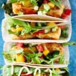 Photo of four tortillas stuffed with crispy tofu, mango, tomato, cucumber and lettuce on a blue plate