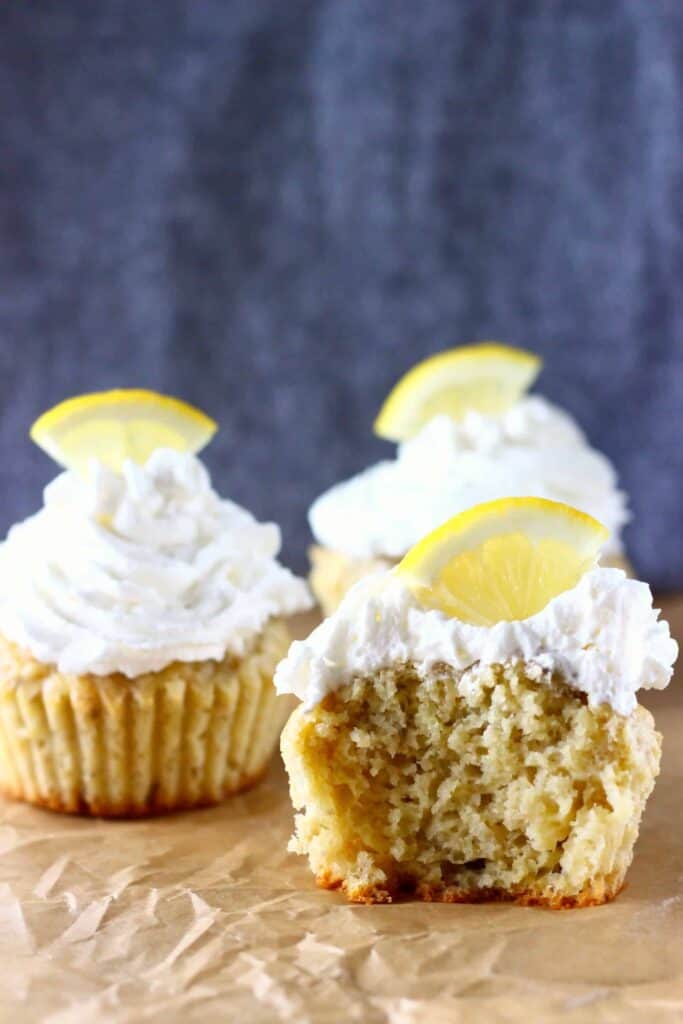 Three lemon cupcakes topped with frosting and lemon slices, one with a bite taken out of it