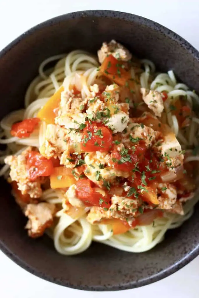 Photo of spaghetti in a dark grey bowl topped with tofu crumbles, vegetables and tomato sauce