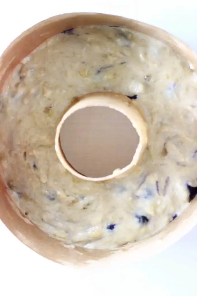 Cake batter dotted with blueberries in a bundt tin on a white background