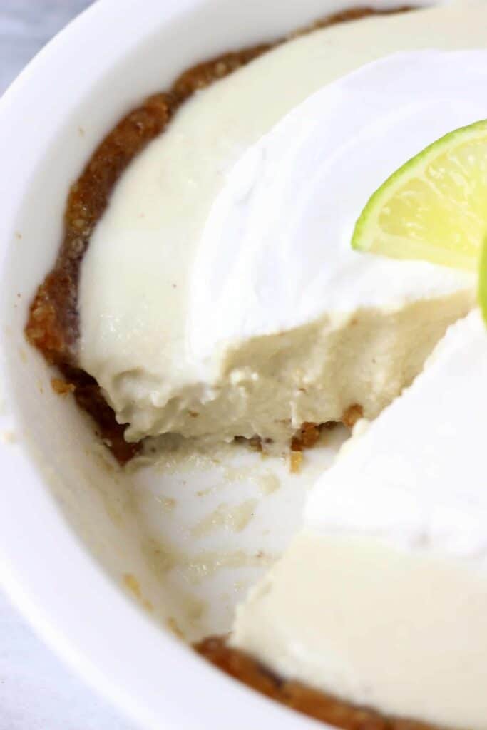 Photo of a pie topped with cream and a lime slice in a pie dish with a slice taken out of it