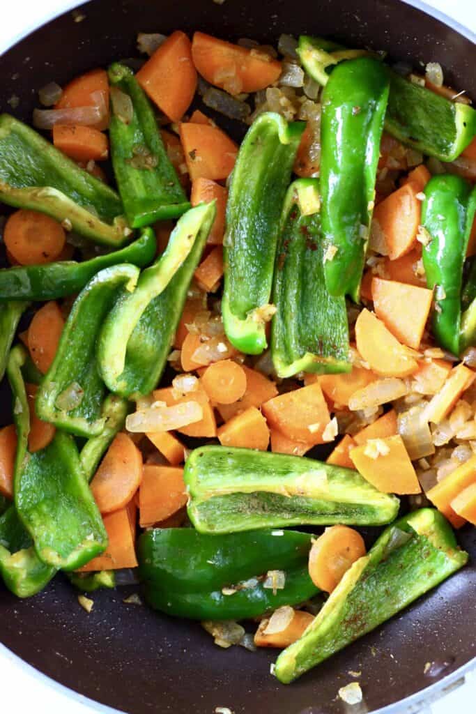 This Vegan Spanish Chickpea Stew is super easy to make, healthy yet satisfying, and packed with veggies! The perfect quick yet nutritious one-pot, plant-based dinner. Gluten-free. #vegan #glutenfree #vegetarian #dairyfree Photo of onions, carrot and green peppers being cooked in a large saucepan