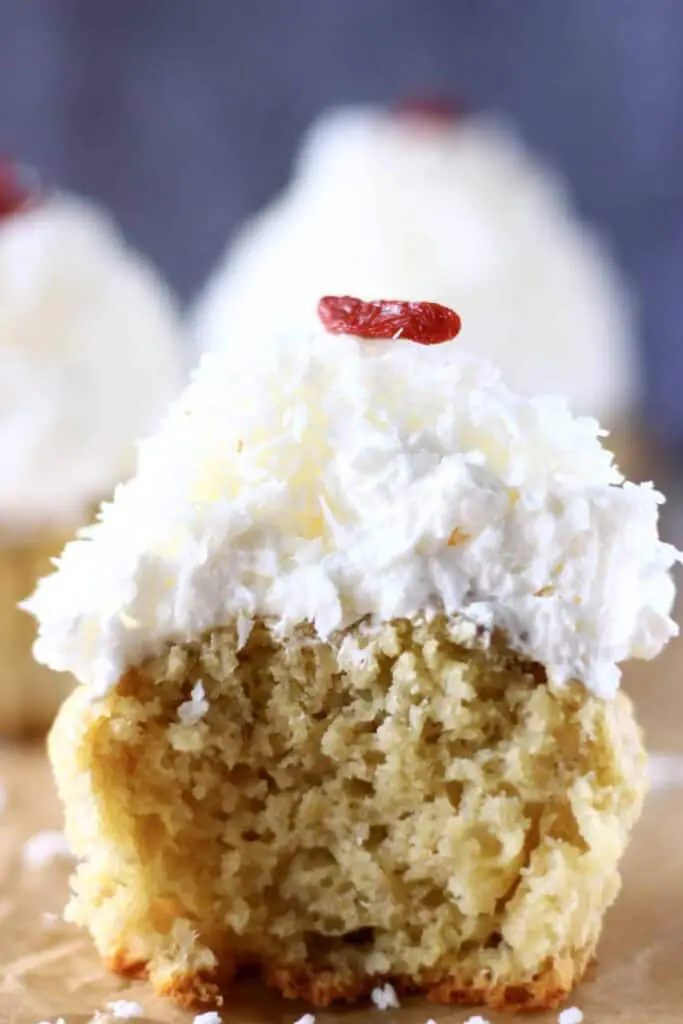 Three cupcakes topped with white frosting, one with a bite taken out of it