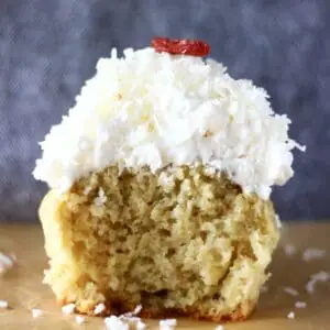 Photo of a cupcake topped with white frosting with a bite taken out of it against a grey background