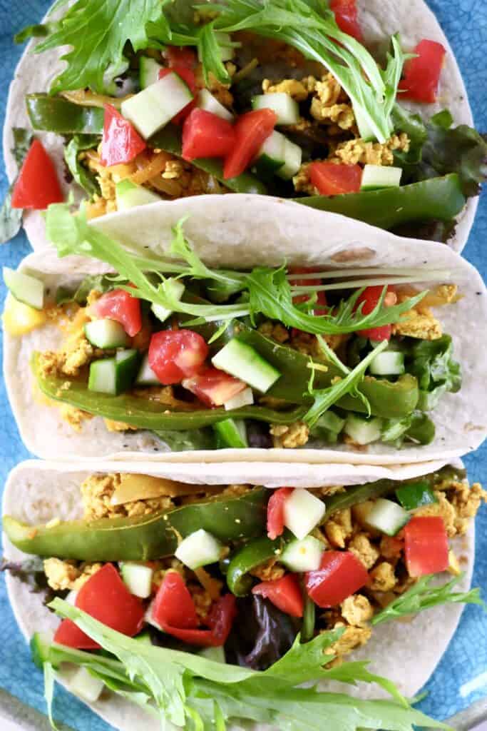 Photo taken from above of three tacos filled with scrambled tofu, lettuce, cucumber and tomatoes